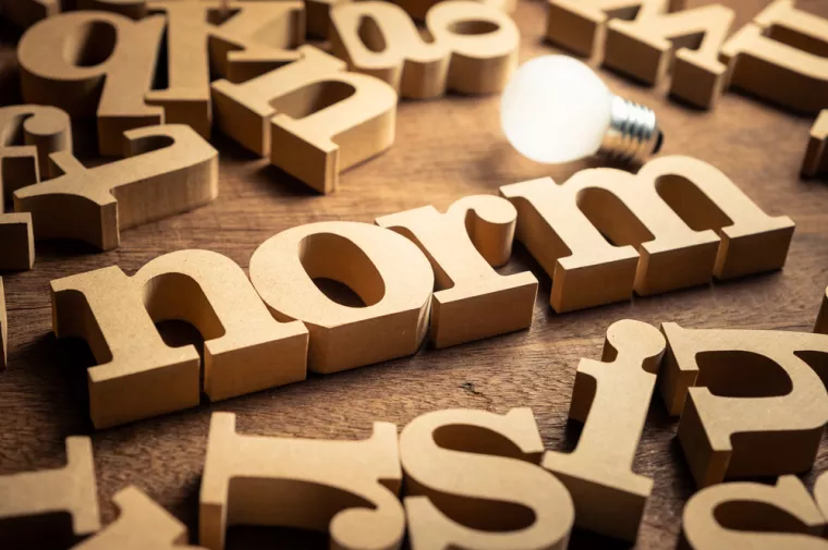 NORM word by wood alphabets with many random letters around and glowing light bulb<br>norma, norme, pravila, pravilo