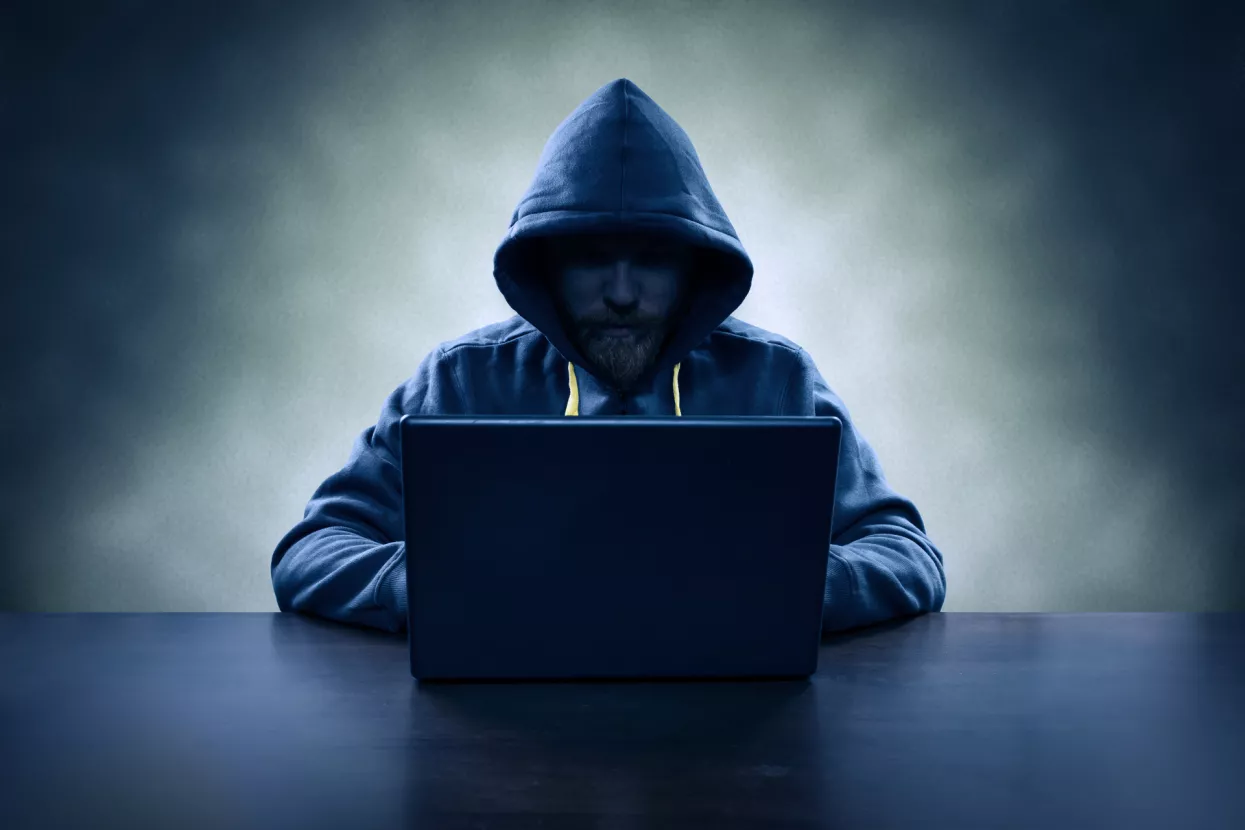 Hooded computer hacker stealing information with laptop