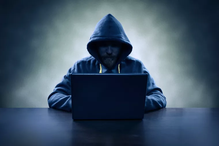 Hooded computer hacker stealing information with laptop