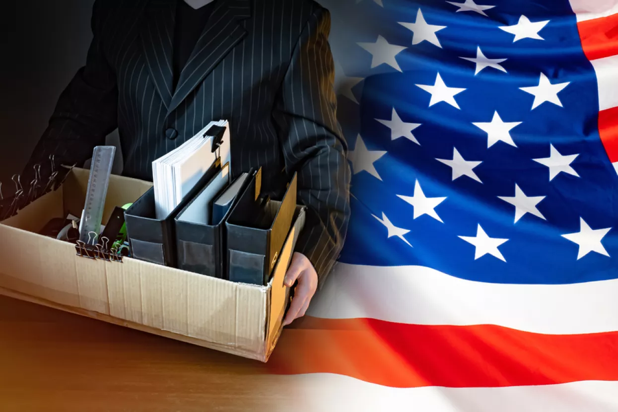 Unemployed. Man holds a box with personal belongings. USA flag. Concept - unemployed American. American was fired. USA resident is unemployed. Stationery in a cardboard box. American labor market amerika<br>sad, zaposlenost, stopa zaposlenosti, posao, poslovi