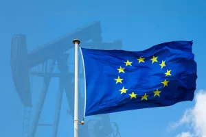 EU flag close-up against the background of an oil pump and a blue sky on a clear day. The concept of oil supplies to Europe.<br>Europa, EU, industrijska proizvodnja, industrija