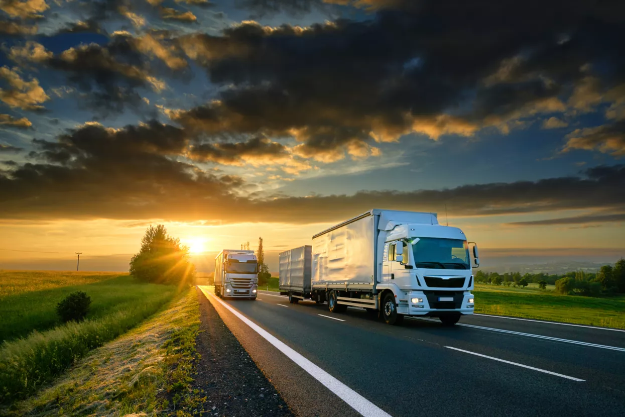 PRILOG<br>Transport, špedicija i izvoznici<br>Overtaking trucks on an asphalt road in a rural landscape at sunset