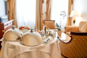 Luxurious Room Service. Breakfast in luxury hotel room delivered by waiter. Meals under silver cloche. Hospitality and vacation concept. Horizontal shot