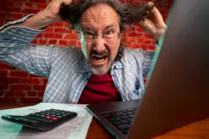 Funny portrait of angry crazy man pulling hair out doing tax prep to balance budget getting debt deficit finding mistake in calculations. Annoyed male count business costs on bankruptcy risk