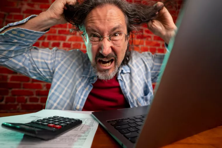 Funny portrait of angry crazy man pulling hair out doing tax prep to balance budget getting debt deficit finding mistake in calculations. Annoyed male count business costs on bankruptcy risk