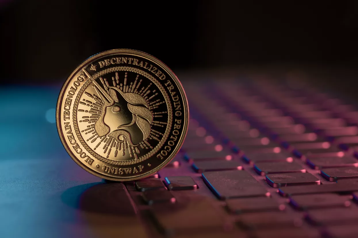 Uniswap UNI cryptocurrency physical coin placed on laptop keyboard and lit with aqua and purple lights
