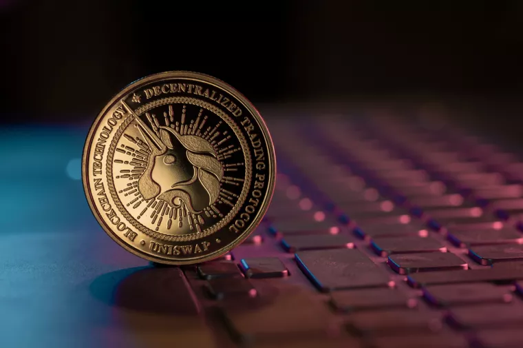 Uniswap UNI cryptocurrency physical coin placed on laptop keyboard and lit with aqua and purple lights