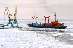 A cargo ship with containers near the pier of the seaport. Maritime navigation and shipping in the Arctic. The ship passes among the ice floes. Anadyr Sea Port, Chukotka, Far East Russia. November.