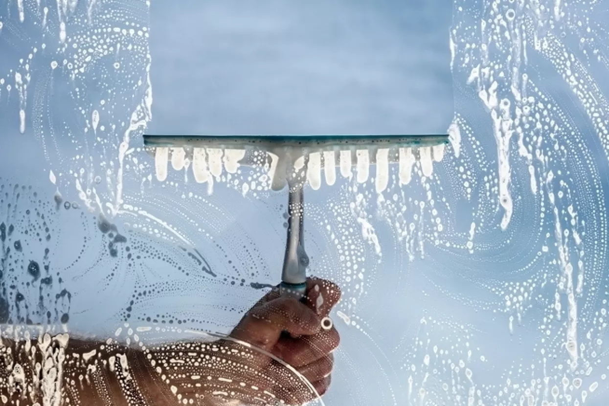 Window cleaner using a squeegee to wash a window with clear blue sky backgroundčišćenje, outsourcing, vanjske usluge, pomoć