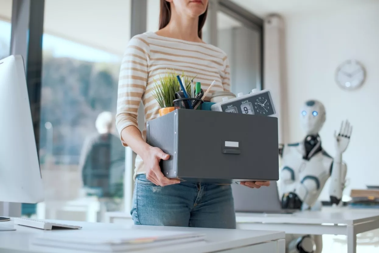 Fired office worker leaving her workplace and humanoid robot staring at herthe impact of AI on employment, silent firing, quiet firing, umjetna inteligencija, radno mjesto, otkaz, otkazi, otpuštanje, AI