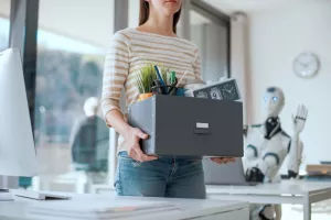 Fired office worker leaving her workplace and humanoid robot staring at herthe impact of AI on employment, silent firing, quiet firing, umjetna inteligencija, radno mjesto, otkaz, otkazi, otpuštanje, AI