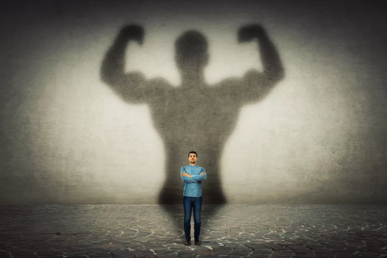 Mali poduzetnikConfident businessman imagine himself a powerful hero, casting shadow of big strong muscular bodybuilder showing his biceps. Inner strength, leadership qualities. Business development.