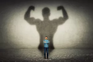 Mali poduzetnikConfident businessman imagine himself a powerful hero, casting shadow of big strong muscular bodybuilder showing his biceps. Inner strength, leadership qualities. Business development.