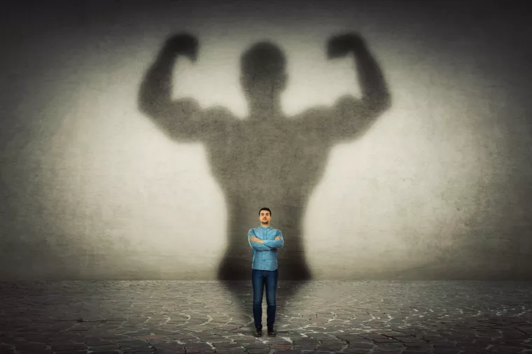 Mali poduzetnikConfident businessman imagine himself a powerful hero, casting shadow of big strong muscular bodybuilder showing his biceps. Inner strength, leadership qualities. Business development.