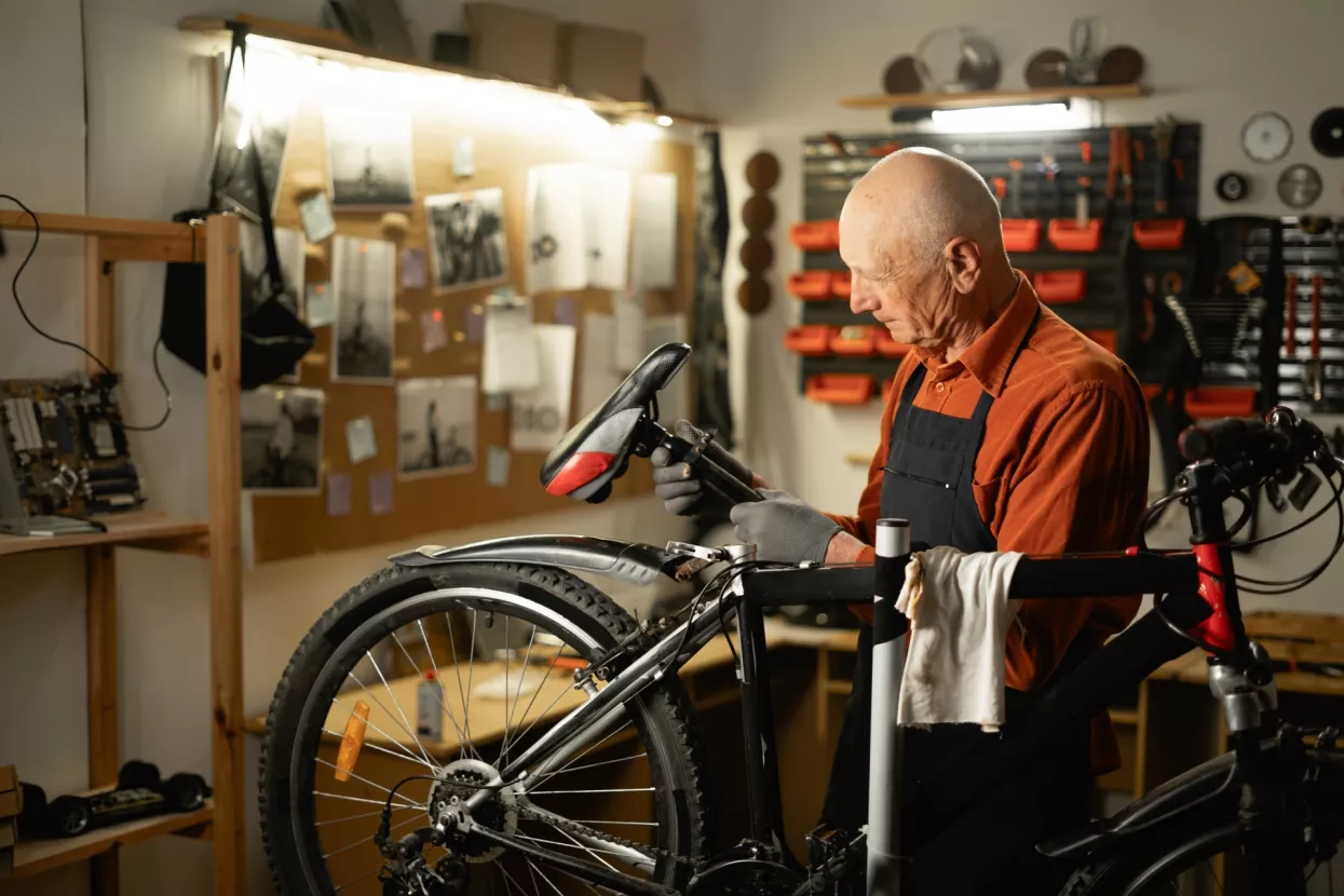 Bike service, repair and upgrade concept. Cycling mechanic fixing bicycle seat in workshop or garage. Old caucasian repairman. Copy space